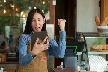 Young businesswoman, owner of an Asian cafe,  navy blue shirt wearing brown apron, looking tablet....