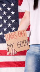 Woman holding a sign Bans Off My Body American flag on background. Protest against anti abortion...