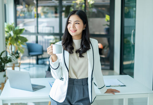Asian businesswoman smiling happily with a new morning holding a cup of coffee lightly sipping coffee professional woman in size working in the office