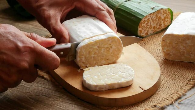a man's hands cutting raw tempeh vegan food