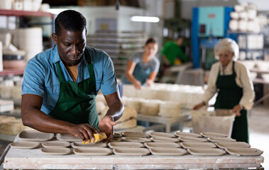 African american man prepares pottery with a foam sponge - removes roughness and unevenness