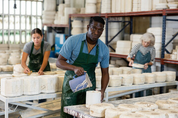 African-american man in apron working in ceramic workshop, pouring clay into mould before firing.