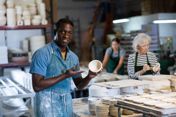 African american male artisan having ceramics in hands and standing in workshop - obrazy, fototapety, plakaty