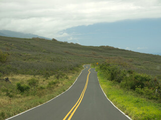 Driving by lonely Maui road with hills and green field on roadside on sunny day, Hawaii