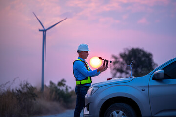 Engineer wearing uniform read blueprint document inspection work in wind turbine farms rotation to electricity,standing in front of car Model windmill and wind force meter is ecology energy concept.