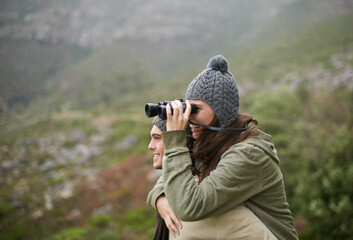 Hiking, binocular and happy couple on piggyback ride, nature exploration and mountain climbing...