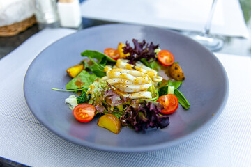 Delicious salad with squid, boiled potatoes and fresh vegetables, served with olive oil
