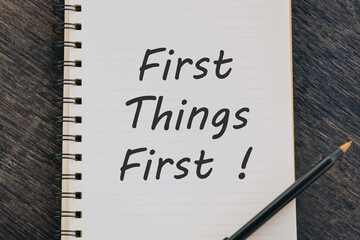 First Things First written on notepad with pen on wooden desk.