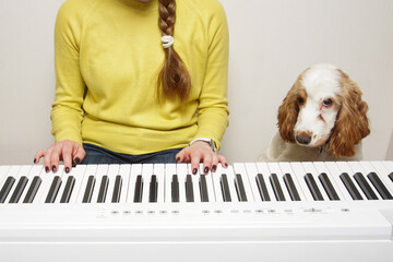 A young woman plays an electronic piano while a dog sitting next to her listens to music.
