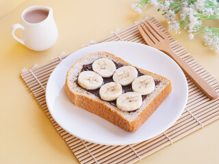 Delicious toasts bread with bananas and chocolate in white plate on beige background. Minimalist product concept