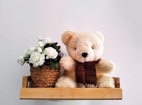 Pictured is a white, green-leafed plastic flower called jasmine placed next to a brown teddy bear used as a symbol of love on Mother's Day in Thailand.