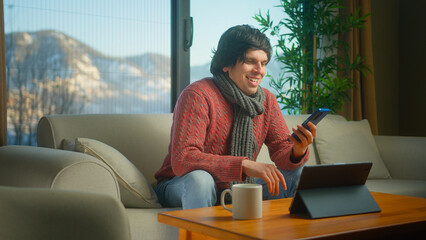 Man sit on sofa surfing internet on mobile phone, checking email, reading media news, scrolling social networks, using mobile applications on smartphone at home