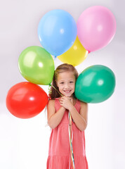 Fototapeta na wymiar Girl, child and birthday balloons in portrait, party decoration and smiling for milestone event in studio. Happy female person, inflatable accessory and joy on white background, playful and celebrate