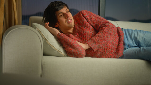 Young man suddenly wakes up while sleeping on couch due to anxiety, disorder, bad dreams and illness or disease. Male trying to sleep in living room at home