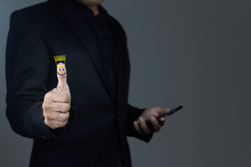 Businessman is using a mobile phone with a thumbs up with a smiley face on it to express great satisfaction on a dark background.