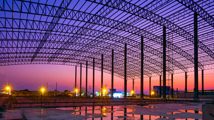 Silhouette curve metal roof beam with columns of large factory building outline structure in construction site at industrial settlement zone against twilight sky background - Powered by Adobe