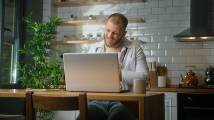 Male doctor wear white uniform with stethoscope having conference video call, chat online with patient through into laptop webcam. Remote medical counselling