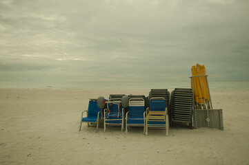 View looking west of multiple Yellow and Blue beach chairs and canopy's stacked in middle with sand in front and Gulf of Mexico in background on a cloudy bright day. At Treasure Island, Florida.	