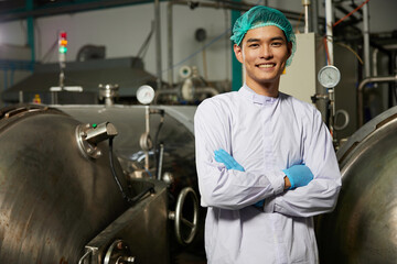 young worker smiling and folded arms pose beside machine control panel or wheel of valve heavy pipe in the factory