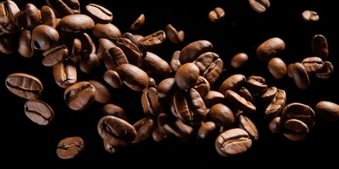 A pile of coffee beans on a black surface. Suitable for coffee shop promotions or food and beverage-related designs