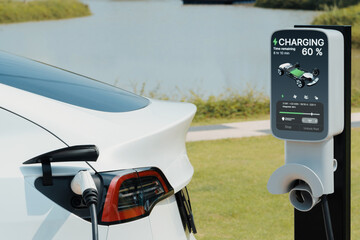 EV electric car recharge battery at parking lot in green city park. Alternative clean energy...