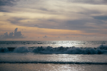 Ocean waves and beautiful sunset sky over horizon. Surfers floating on waves in expectation.