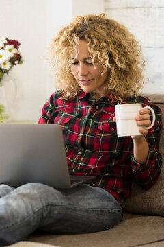 Beautiful adult young woman at home with laptop computer lay down on the couch - concept of alternative office and workstation - modern job with technology and people -  curly long hair