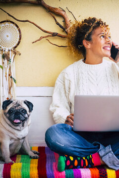 Funny work and technology concept picture with adult cheerful caucasian young beautiful woman calling at the phone and using laptop computer and cute lovely nice dog pug best friend near her