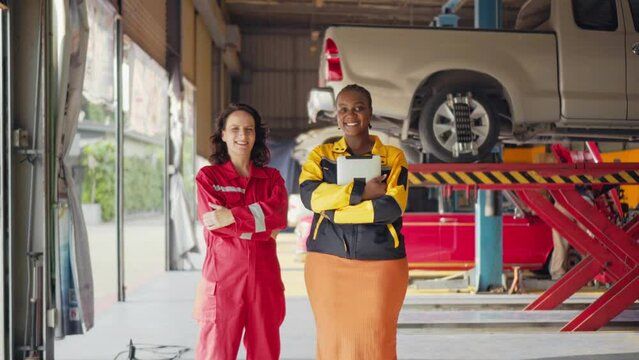 american and caucasian women mechanic skillful worker stand together showing teamwork in the garage . industrial and Factory people and manufacturing labor concept