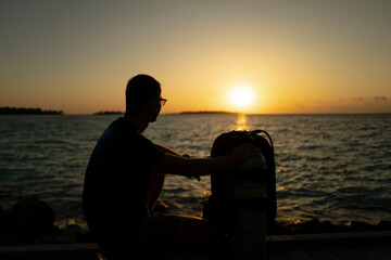 A guy with a scuba kit standing in front of a sunset.