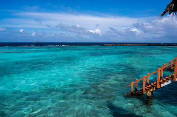 View of the pale blue water of the lagoon. In the background is a dark ocean. On the right, wooden...