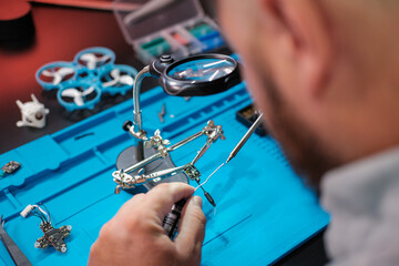 Close-up of a male engineer's hands soldering a video transmitter chip from an FPV drone using a...