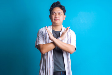 Young Asian male making stop gesture with hand giving advice to avoid danger on blue background