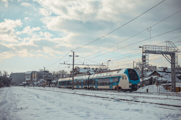 Modern white and blue commuter double decker train is driving through the suburbs of Ljubljana on a cold winter day. Passenger commute in winter, snow and cold