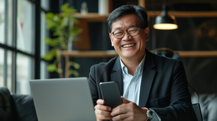 Fototapeta premium Senior middle aged Asian businessman manager ceo using smartphone and laptop in office working online