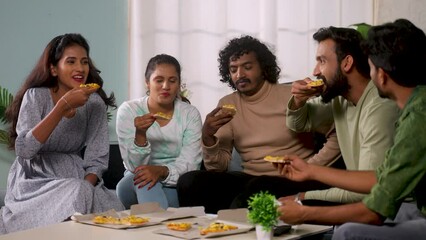 Group of joyful young group of friends enjoys eating pizza during home gathering - concept of weekend meetup, bonding friendship and recreation