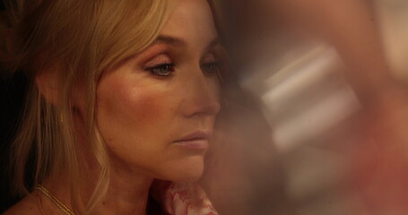 Portrait of a beautiful blonde standing in front of a mirror, looking at her clothes and fixing her make-up. Close-up of a woman's face in front of a mirror.