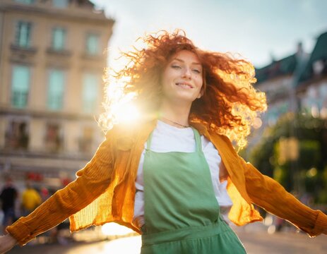 Mujer cauc&aacute;sica y pelirroja, bailando en la calle en un atardecer con el sol a su espalda