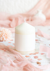Obraz na płótnie Canvas Candle with blank label near pink decorations, hearts and tulle on white table close up, mockup