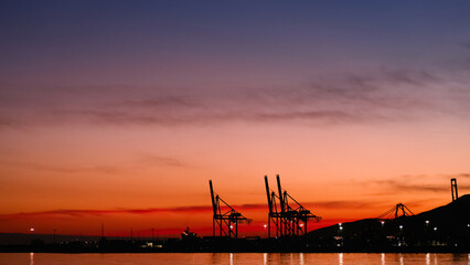 Obraz premium Sunset sky by the sea beach with silhouette harbour and blurry twilight Dusk sky in Evening in orange, red, purple, blue with cloud,Horizon Nature Golden Sky,Beautiful Sunrise background