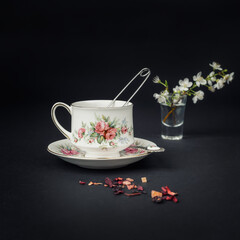 Still life with a beautiful fine china tea cup and tea accessories on a black background