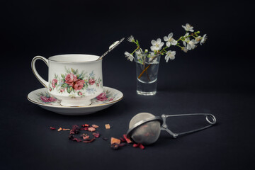 Still life with a beautiful fine china tea cup and tea accessories on a black background