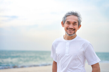 portrait happy asian senior man travel in nature,smiling and standing on the beach on summer time,concept of elderly pensioner lifestyle,holiday,travel,wellness,wellbeing