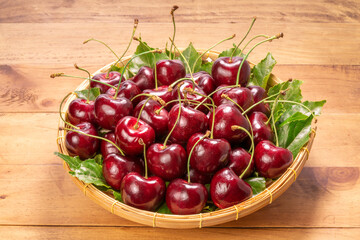 Sweet Red cherry in bamboo basket on wooden background, Red cherry with leaf on table.