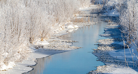 The river flows in winter along frozen snow-covered banks.
