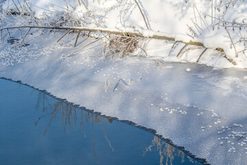 The river flows in winter along frozen snow-covered banks.