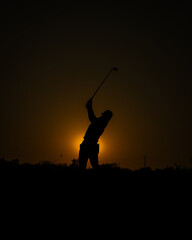 silhouette of a golfer swinging in the afternoon setting sun