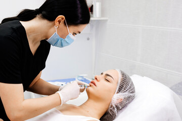 A cosmetologist makes injections into the lips of a beautiful girl. Procedure for lip augmentation,...