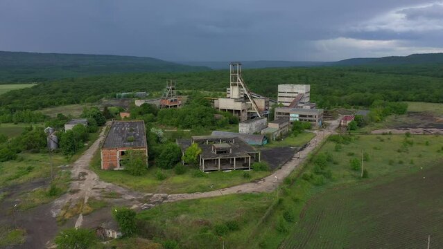 Aerial drone view of old abandoned overgrown coal mine. The shaft tower and desolate concrete buildings of mining factory. Decarbonization, green deal in the modern world during the energy crisis.