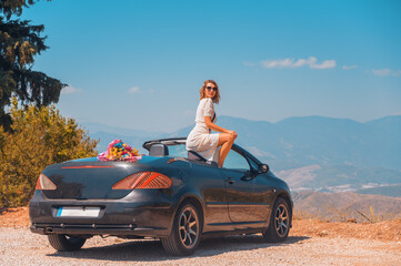 Happy newlyweds on their honeymoon in a beautiful convertible car posing against the backdrop of...